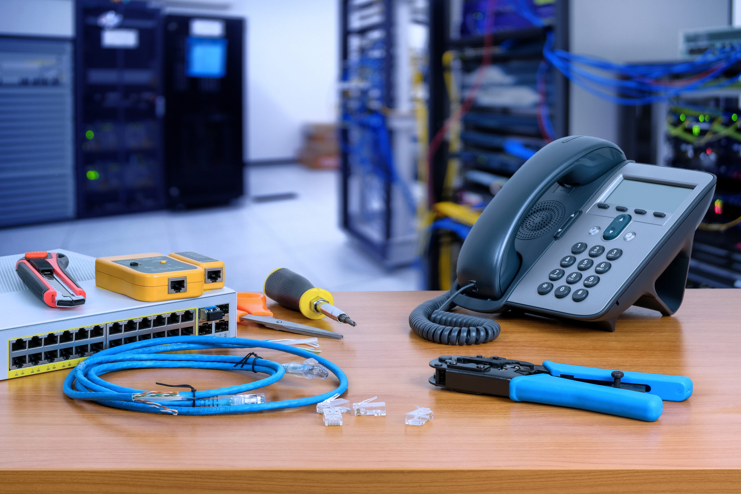 device for network system on table. network gigabit switch, crimping pliers, tester tool and IP Telephone and blur data center room background